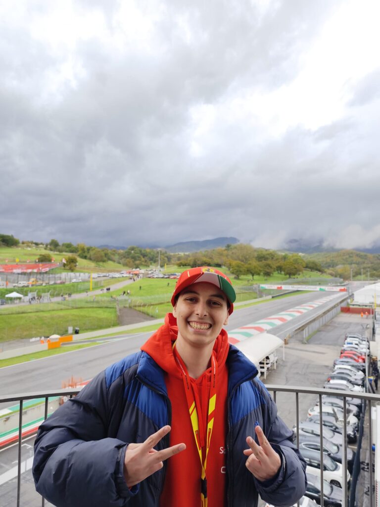 Salvatore sorride davanti a una monoposto di Formula 1 esposta all’aperto, indossando una maglia bianca e un cappellino, durante una giornata evento legata al mondo dei motori.